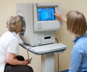 To kvinner ved et apparat som brukes til synsfeltmåling. Den ene ser på en dataskjerm.