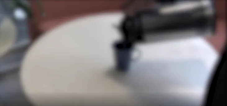 Bilde av bord, kaffekopp og noen som heller kaffe koppen. Bildet er gjort uskarpt.