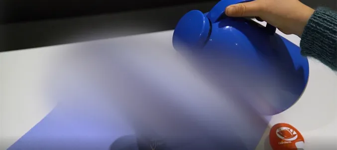 Bilde av bord, kaffekopp og noen som heller kaffe koppen. Bildet er uskarpt på midten.