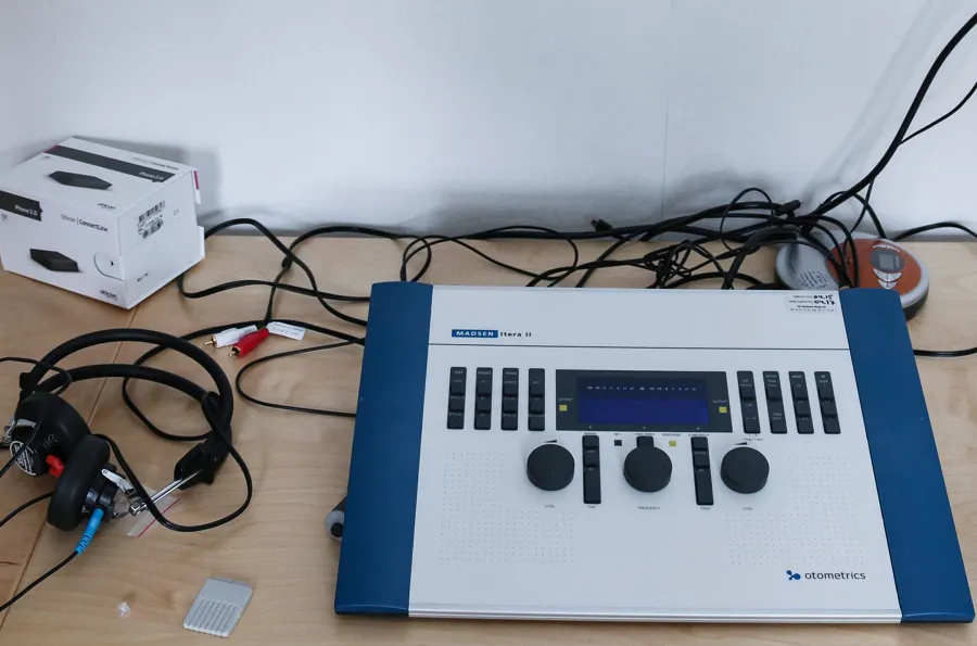 En hvit boks med runde skruhjul, knapper og en skjerm. Rundt på bordet ligger det ledninger og en hodetelefon.