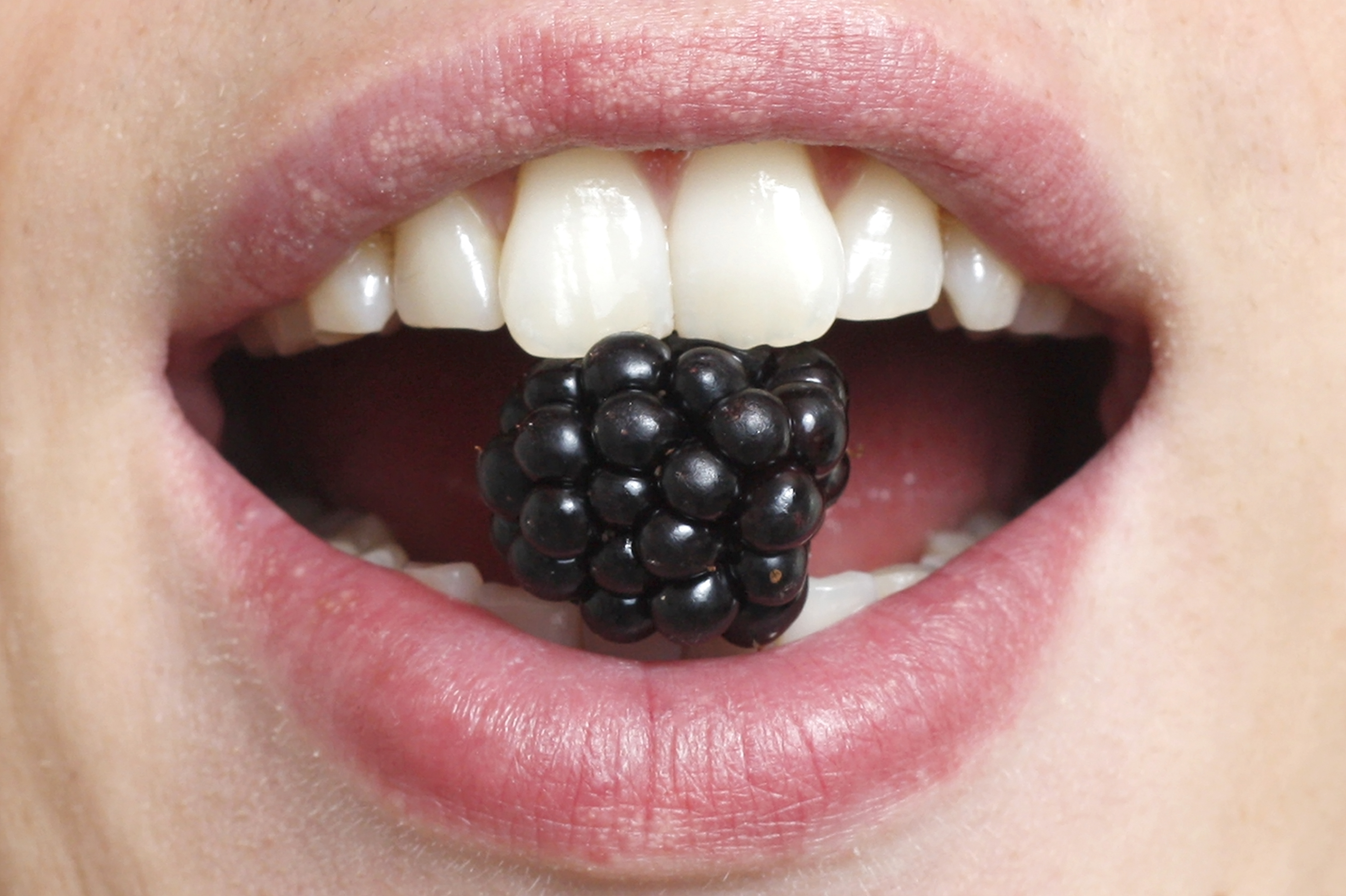Nærbilde av munn som har et svart bær mellom tennene.