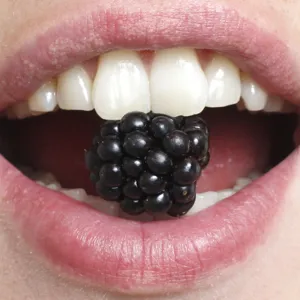 Nærbilde av munn som har et svart bær mellom tennene.