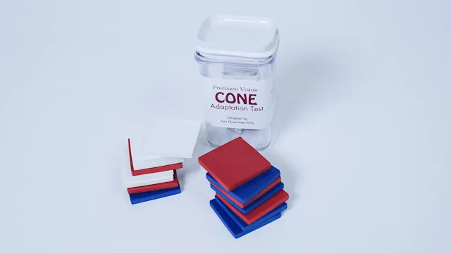 Bilde av små firkant papirlapper i blått, hvitt og rødt plassert opp på hverandre. I bakgrunnen en plastboks med skrift på.