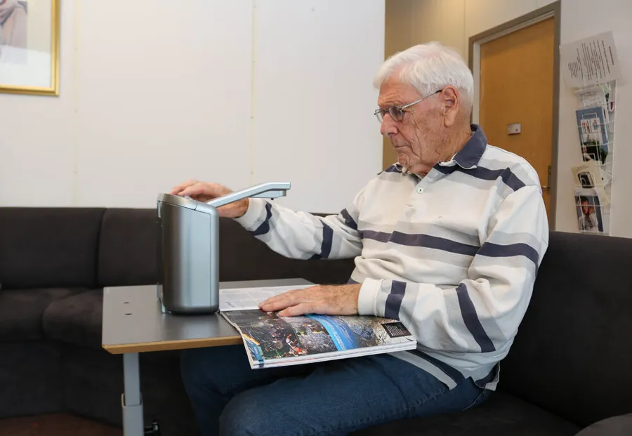 En mann som sitter og leser et blad med lesemaskin.