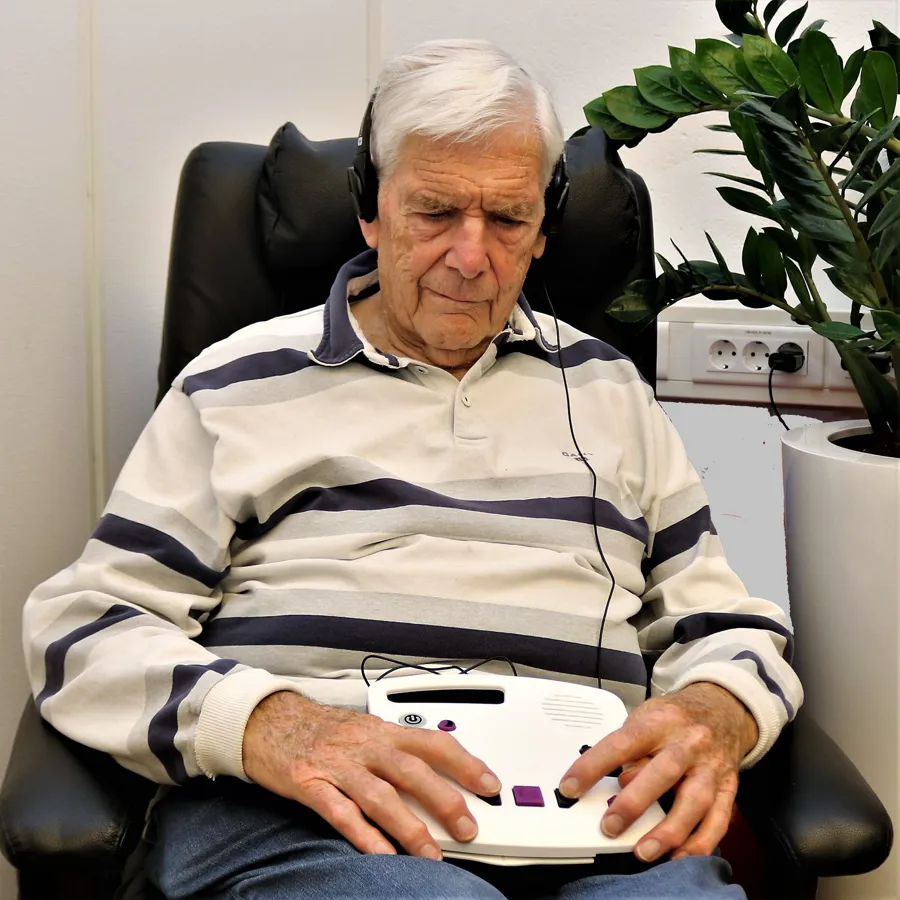 En mann som sitter i en stol og leser en bok med DAISY-spiller.